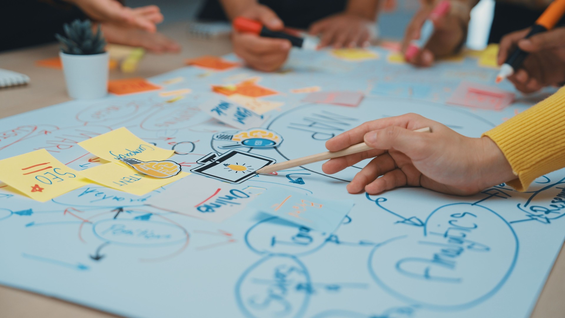 Group of people brainstorming and collaborating on project ideas with colorful sticky notes on large paper in a modern office space SACTR